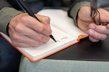 Detail-Foto des Gründers von make possible marc keller mit fokus auf seine hände mit einem stift beim schreiben in ein notizbuch